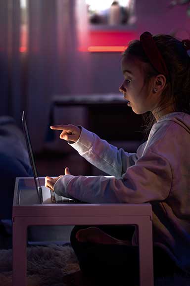 Menina olhando e apontando para computador com expressão de surpresa