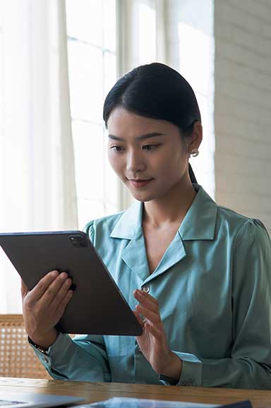 Mulher oriental de camisa social, olhando para tablet