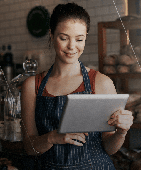 Mulher com avental sorrindo enquanto trabalha no tablet